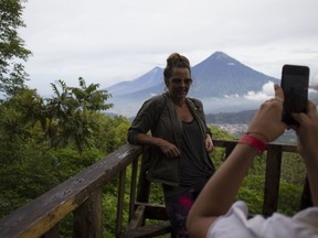 In this June 8, 2018 photo, a tourist poses for a photograph from a lookout point on ascent to the summit of the Pacaya volcano in San Francisco de Sales, Guatemala. Tourists come to Pacaya for the altitude, cool weather, stunning views and singular experience of seeing the force of nature.