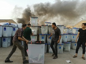 Iraqi electoral officials work to salvage ballot boxes as smoke rises from a fire that broke out at Baghdad's largest ballot box storage site, where ballots from Iraq's May parliamentary elections are stored, in Baghdad, Iraq, Sunday, June 10, 2018.