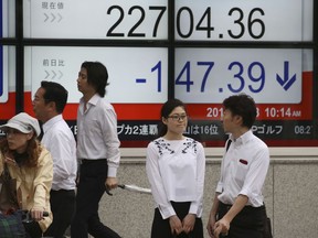 People stand by an electronic stock board of a securities firm in Tokyo, Monday, June 18, 2018. Asian shares were mostly lower Monday amid worries about trade tensions as the U.S. and China both started putting tariffs in motion. China and Hong Kong markets were closed for a national holiday.