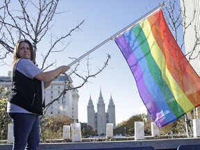 FILE - In this Nov. 14, 2015, file photo, Sandy Newcomb poses for a photograph with a rainbow flag as Mormons gather for a mass resignation from the Church of Jesus Christ of Latter-day Saints in Salt Lake City. The Mormon church's massive genealogical database will begin accepting submissions of names of people from same-sex relationships sometime next year. The move doesn't foreshadow any change to long-standing church opposition to gay marriage, but it is being done to ensure the databank has as much information as possible for researchers, according to a statement from The Church of Jesus Christ of Latter-day Saints.