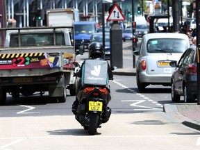 A Deliveroo driver is seen in traffic in north London, Friday, June 15, 2018. A judge has given a British union permission to mount a legal challenge over the employment status of drivers for the food-delivery service Deliveroo. Last year a tribunal ruled that Deliveroo's moped drivers and cyclists are self-employed. The Independent Workers Union of Great Britain disputes that and says riders are being "denied basic employment rights" including a guaranteed minimum wage, holiday pay and collective-bargaining rights.