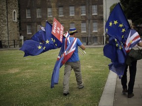 In this photo taken Wednesday, June 20, 2018, anti-Brexit, pro-EU supporters walk with EU and Union flags, with a placard near the Houses of Parliament in London. The divisions opened up by the 2016 referendum have not healed, but hardened, splitting Britain into two camps: leavers and remainers. Almost the only thing the two groups share is pessimism about the way Brexit is going.