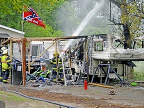 In this Monday, June 11, 2018 photo, Bronson firefighters wet down a smoldering tree at the scene of a fatal fire in Bronson, Mich. Authorities say there's no indication of foul play in the camper fire in southern Michigan that killed two young siblings and a dog and injured a third child.