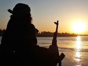 In this photo released on Sept. 29, 2014 by a militant website an ISIL fighter holds his AK-47 machine gun as he relaxes on the bank of the Euphrates river in Raqqa, Syria.