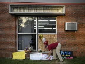 FILE - In this Aug. 8, 2017 file photo, Ben Sunderlin places a sign of support near the window that was damaged during Saturday morning's attack at the Dar Al-Farooq Islamic Center in Bloomington, Minn. A grand jury added federal civil rights and hate crimes violations to the charges three Illinois men face in the bombing of a mosque in suburban Minneapolis, prosecutors announced Thursday, June 21, 2018.