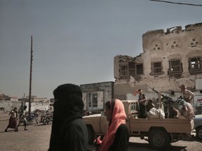 In this Feb. 12, 2018, photo, women walk past Saudi-led coalition backed forces, leading the campaign to take over Hodeida, as they patrol Mocha, a port city on the Red Sea coast of Yemen. Violence, famine and disease have ravished the country of some 28 million, which was already the Arab world's poorest before the conflict began. The conflict pits a U.S.-backed, Saudi-led coalition supporting the internationally recognized government, which has nominally relocated to Aden but largely lives in exile, against rebels known as Houthis.