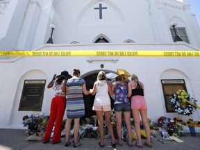 FILE - In this June 18, 2015, file photo, a group of women pray together at a makeshift memorial on the sidewalk in front of the Emanuel AME Church, in Charleston, S.C.  A judge dismissed a lawsuit, June 18, 2018, against the FBI for a faulty background check that allowed Dylann Roof to buy the gun he used to kill nine people in a racist attack at a South Carolina church.  U.S. District Judge Richard Gergel also blasted the federal government's "abysmally poor policy choices" in running the database for firearm background checks.
