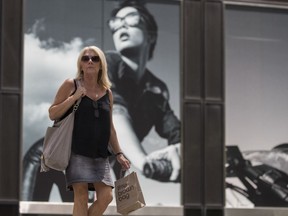 In this June 20, 2018, photo, a pedestrian walks carrying a Bloomingdales' Little Brown Bag walks past a giant advertisement for Armani Exchange on Fifth Avenue in New York. On Tuesday, June 26, the Conference Board releases its June index on U.S. consumer confidence.