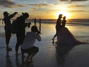 FILE- In this Jan. 18, 2017, file photo, photographers take photos of a tourist couple's wedding at the famous Kuta beach during sunset in Bali, Indonesia. According to a 2016 survey from wedding site The Knot, the average cost of an international destination wedding is $25,800. That figure may be within your event budget, but for guests, international airfare and multinight lodging could be out of reach.