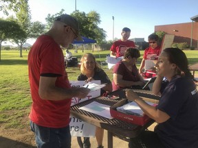 In this June 5, 2018, photo, mathematics teacher Heather LaBelle, seated right, shows Roger Baker, left, how to gather signatures for the Invest in Education Act, a proposal to raise money on high earners to fund public education in Phoenix, Ariz. LaBelle, like many of the teachers in the #RedforEd movement that triggered a six-day statewide teacher walkout, says while improving teacher pay is one step toward better schools, more funding is needed for public education.