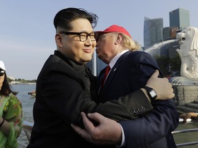 A tourist looks on as Kim Jong Un and Donald Trump impersonators, Howard X, center, and Dennis Alan, right, embrace during their visit to the Merlion Park, a popular tourist destination in Singapore, on Friday, June 8, 2018.