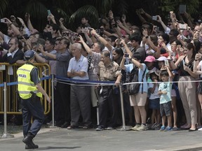 Curious onlookers wait for the departure of the motorcade of U.S. President Donald Trump from the Istana or Presidential Palace in Singapore on Monday, June 11, 2018, as Trump met Singapore Prime Minister Lee Hsien Loong ahead of the summit with North Korea leader Kim Jong Un.