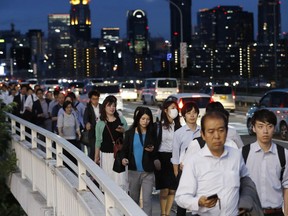 In this June 18, 2018, photo, people walk on a bridge while train and subway service were suspended to check for damage after an earthquake in Osaka, western Japan. The magnitude 6.1 earthquake that struck the area early Monday damaged buildings and left many homes without water or gas. The quake also grounded flights in and out of Osaka and paralyzed traffic and commuter trains most of the day.