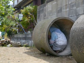 In this June 12, 2017, photo, an elderly resident takes shelter in a concrete culvert during an evacuation drill in the wake of North Korea's repeated launches of ballistic missiles, in Tsubame, Niigata prefecture, northwest of Tokyo. Cabinet Secretariat in charge of crisis management said Thursday, June 21, 2018, Japan plans to suspend civilian evacuation drills planned for the rest of the year amid easing tension following the U.S.-North Korea summit. (Kyodo News via AP)