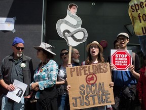 A woman holds a sign with a drawing of Prime Minister Justin Trudeau's face on a snake as protesters opposed to the Kinder Morgan Trans Mountain pipeline extension demonstrate outside Justice Minister Jody Wilson-Raybould's constituency office, in Vancouver, on Monday June 4, 2018.