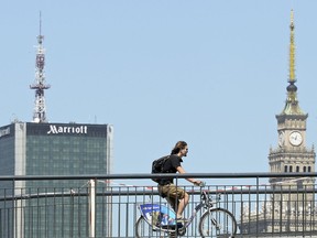 In this May 29, 2018 photo a cyclist rides on a bike path bridge in front of a new hotel and the old Communist Palace of Culture in Warsaw, Poland. Warsaw, a city of Old World charm that was turned to rubble and ash by Nazi Germany, has been reborn twice. The Polish capital first became an example of socialist city planning, rising in the postwar era as a drab and grey embodiment of oppressive Communist rule. But almost three decades of post-communist economic growth have produced a booming city of modern glass architecture, cutting-edge museums and revitalized historic buildings.