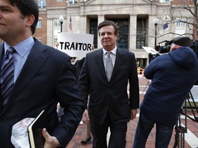 FILE - In this March 8, 2018, file photo, Jason Maloni, left, former Trump campaign chairman Paul Manafort's spokesman, left, walks with Paul Manafort, center, as they leave the Alexandria Federal Courthouse after an arraignment hearing in Alexandria, Va. A federal judge in Virginia has rejected Manfort's move to throw out charges brought by the special counsel in the Russia investigation. The decision June 26 was a setback for Manafort in his defense against numerous tax and bank fraud charges. Behind Manafort protester Bill Christeson holds up a sign that says "traitor."