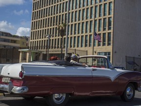 FILE - In this Oct. 3, 2017, file photo, tourists ride a classic convertible car on the Malecon beside the United States Embassy in Havana, Cuba. Medical tests have confirmed that one additional U.S. Embassy worker has been affected by mysterious health incidents in Cuba, bringing the total number to 25. That's according to an unclassified notice sent to congressional officials by the State Department.