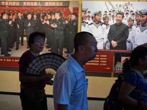 FILE - In this Aug. 1, 2017, file photo, visitors walk past photos of Chinese President Xi Jinping visiting troops during an exhibition to mark the 90th anniversary of the founding of the People's Liberation Army at the military museum in Beijing. On Chinese state television broadcasts, President Xi Jinping is often shown clad in battle fatigues inspecting troops, praising their service, and hailing the People's Liberation Army as key to the country's rising global power. But the nationalist drumbeat rings hollow for many retired soldiers who feel left behind, and they have taken to the streets in droves on last week to complain about having to fend for themselves with meager pensions and little support. The unrest poses a delicate political challenge for Xi, who has made his affinity for the military one of the pillars of his folksy image.
