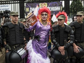 A gay and lesbian rights activist stands between Ukrainian police guards during the annual Gay Pride parade, protected by riot police in Kiev, Ukraine, Sunday, June 17, 2018. Several thousand supporters of gay pride have held a march in Ukraine's capital that lasted about 20 minutes despite opponents attempts to block them.