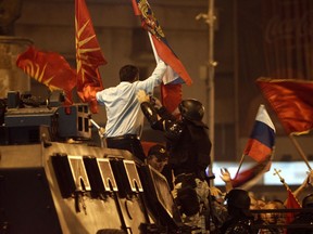 A police officer tries to grab a protester waving former Macedonian and Russian flags atop of a police vehicle during a protest of opponents of the deal between Greece and Macedonia on the latter country's new name "North Macedonia", outside the parliament in Skopje, Macedonia, Sunday, June 17, 2018. The preliminary deal signed by the two countries' foreign ministers in the Prespes Lakes area, Greece, launches a long process that will last several months. If successful, it will end a decades-long dispute between neighbors Greece and Macedonia, which will be renamed North Macedonia.