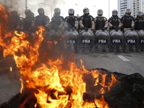 Police stand guard where striking protesters use burning tires to block a road the leads to the city from the south, in Buenos Aires, Argentina, Monday, June 25, 2018. A strike led by Argentina's largest union confederation to protest the economic austerity policies of President Mauricio Macri has shut down much of the country's capital _ freezing public transportation, airlines, ports, schools, banks and government offices.