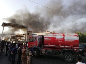 Iraqi security forces and firemen gather as smoke rises from a fire that broke out at Baghdad's largest ballot box storage site, where ballots from Iraq's May parliamentary elections are stored, in Baghdad, Iraq, Sunday, June 10, 2018. The ballots are part of a manual recount of votes, mandated in a law passed by the Iraqi parliament last Wednesday.