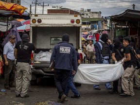 FILE - In March 15, 2017 file photo, police investigators carry a body to a forensic vehicle, after a shootout between private security guards and gang members, at the central market in San Salvador, El Salvador, Wednesday, March 15, 2017. The rate of violent death in El Salvador is still higher than all countries suffering armed conflict except for Syria.