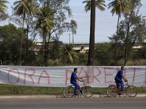 Workers pedal their bicycles past a banner with a message that reads in Portuguese: "Get out Parente", in reference to  Pedro Parente, the president of the state-owned oil company, at the entrance of a Petrobras refinery during a strike in Duque da Caxias, Brazil, Wednesday, May 30, 2018. Brazilian oil workers began a 3-day strike to demand a drop in the price of cooking gas.