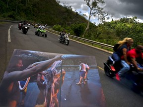 A printed photograph taken on Sept. 28, 2017 shows people bathing on the highway after Hurricane Maria destroyed people's homes, held up at the same spot of the highway where motorcyclists ride past in Naranjito, Puerto Rico, May 27, 2018. Thanks to the owners of the land alongside the highway, creek water was piped to the side of the road for people without water to use for bathing, washing clothes and dishes.