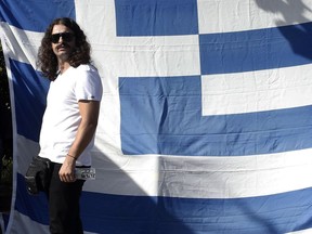 FILE - In this Tuesday, Oct. 1, 2013 file photo, Lawmaker of the extreme far-right Golden Dawn party Costas Barbarousis, stands in front of a Greek flag during a protest in Athens. Greek anti-terrorism police in Athens have arrested an extreme far-right lawmaker on treason-linked charges, more than two days after he evaded arrest by speeding past a series of police highway checkpoints, it was reported on Monday, June 18, 2018.  Barbaroussis has been charged with committing preparatory acts for high treason over his exhortations for the armed forces to arrest the country's leadership, to hinder a deal with neighboring Macedonia over that country's name.