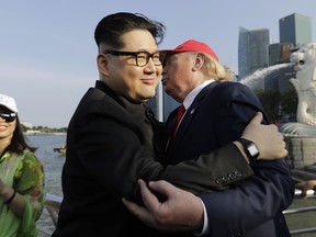 A tourist looks on as Kim Jong Un and Donald Trump impersonators, Howard X, center, and Dennis Alan, right, embrace during their visit to the Merlion Park, a popular tourist destination in Singapore, on Friday, June 8, 2018. Kim Jong Un lookalike who uses the name Howard X said he was detained and questioned upon his arrival in Singapore on Friday, days before a summit between the North Korean leader and President Donald Trump.