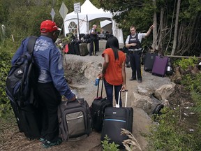 In this Aug. 7, 2017 file photo, a Royal Canadian Mounted Police officer informs a migrant couple of the location of a legal border station, shortly before they illegally crossed from Champlain, N.Y., to Saint-Bernard-de-Lacolle, Quebec, using Roxham Road.