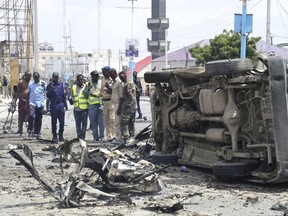 Somali forces watch a vehicle demolished by twin blast in Mogadishu on Saturday, July, 7, 208.  At least nine people have been killed and many others injured in an ongoing attack at Somalia's interior ministry as security forces continued battling militants holed up inside, Somali officials say.