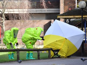 In this file photo taken on March 8, 2018 members of the emergency services in green biohazard encapsulated suits afix the tent over the bench where where Ex-Russian spy Sergei Skripal and his daughter Yulia were found on March 4 in critical condition.