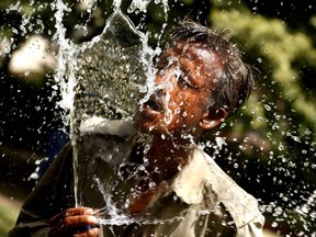 An man cools himself by splashing water from a pipe on a hot summer day in Allahabad, India, on Sunday, May 27, 2012.