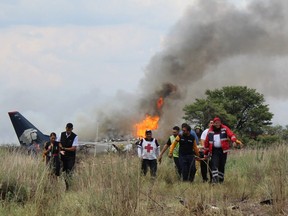 In this photo released by Red Cross Durango communications office, Red Cross workers and rescue workers carry an injured person on a stretcher, right, as airline workers, left, walk away from the site where an Aeromexico airliner crashed in a field near the airport in Durango, Mexico, Tuesday, July 31, 2018.