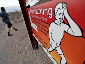 In this Tuesday, July 24, 2018 photo, a hiker walks past a heat warning sign at sunrise, in Phoenix. Already devilishly hot for being in the Sonoran desert, Arizona's largest city is also an "urban heat island," a phenomenon that pushes up temperatures in areas covered in heat-retaining asphalt and concrete. Phoenix officials say they are tackling urban warming, monitoring downtown temperatures, planting thousands of trees and capturing rainwater to cool off public spaces.