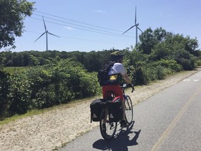 In this Friday, July 13, 2018 photo provided by Lori Riley, Associated Press reporter Pat Eaton-Robb rides past windmills on the Phoenix Trail in Fairhaven, Mass. The trail is part of the East Coast Greenway, a planned 3,000-mile collection of trails from Maine to Florida which is about 41 percent complete in southern New England.