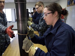 FILE - In this April 26, 2017 file photo, U.S. Navy Ensign Megan Stevenson, right, of Raymond, Maine, trains at patching high-pressure pipe leaks during a class at the Naval Submarine School, in Groton, Conn. The Navy said Tuesday, July 10, 2018, it will let women sailors sport ponytails and other longer hairstyles, reversing a policy that long forbade females from letting their hair down.