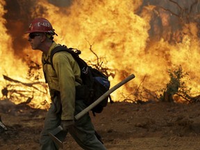 A firefighter walks along a containment line in front of an advancing wildfire Saturday, July 28, 2018, in Redding, Calif.