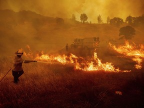 A firefighter scrambles to stop a wildfire as wind drives embers across Highway 20 near Clearlake Oaks, Calif., on Sunday, July 1, 2018.