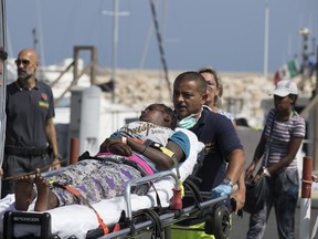 A woman is carried away on a stretcher after disembarking from an Italian Coast Guard ship in the port of Pozzallo, Southern Italy, Sunday, July 15, 2018. Another day's worth of food and beverages was sent Sunday to a pair of military ships off Sicily as Italy waited for more European nations to pledge to take a share of the hundreds of migrants on board before allowing the asylum-seekers to step off onto Italian soil.