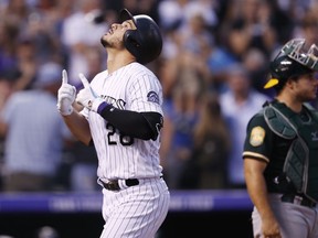 Colorado Rockies' Nolan Arenado, left, gestures as he crosses home plate after hitting a solo home as Oakland Athletics catcher Josh Phegley looks on in the third inning of a baseball game Saturday, July 28, 2018, in Denver.