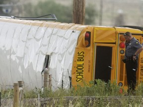 A Weld County Sheriffs Deputy talks on the phone at the scene of a crash involving a school bus after it flipped near the intersection of Weld County Road 49 and Weld County Road 24 near Hudson, Colo., Thursday, July 12. 2018. Authorities say multiple people were injured when the school bus carrying 35 high school students crashed and tipped over on the rural road northeast of Denver.
