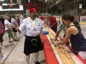 Chef Alain Bosse stands next to a lobster roll measuring measured just over 67 metres in Shediac, N.B., in this Wednesday, July 4, 2018 handout photo. It took the will and work of dozens of people, buckets of seasoned meat and a room big enough to accommodate what is being heralded as the world's longest lobster roll.