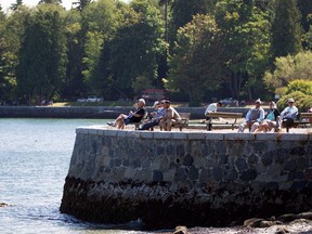People sit along the Stanley Park seawall as others fish in Vancouver, B.C., on Sunday, August 25, 2013.