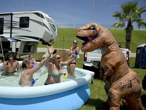 Joseph Gullett, right, dressed in a dinosaur suit jokes with fans relaxing in a pool cooling off in a camping area before a NASCAR cup series auto race at Daytona International Speedway, Saturday, July 7, 2018, in Daytona Beach, Fla.