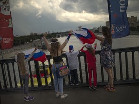 People wave Russian flags on the Krymsky Bridge to passengers aboard a ferry on the Moskva river in Moscow, Russia, Sunday, July 1, 2018.