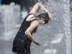 A woman cools down in a water fountain as she beats the heat in Montreal, Monday, July 2, 2018.